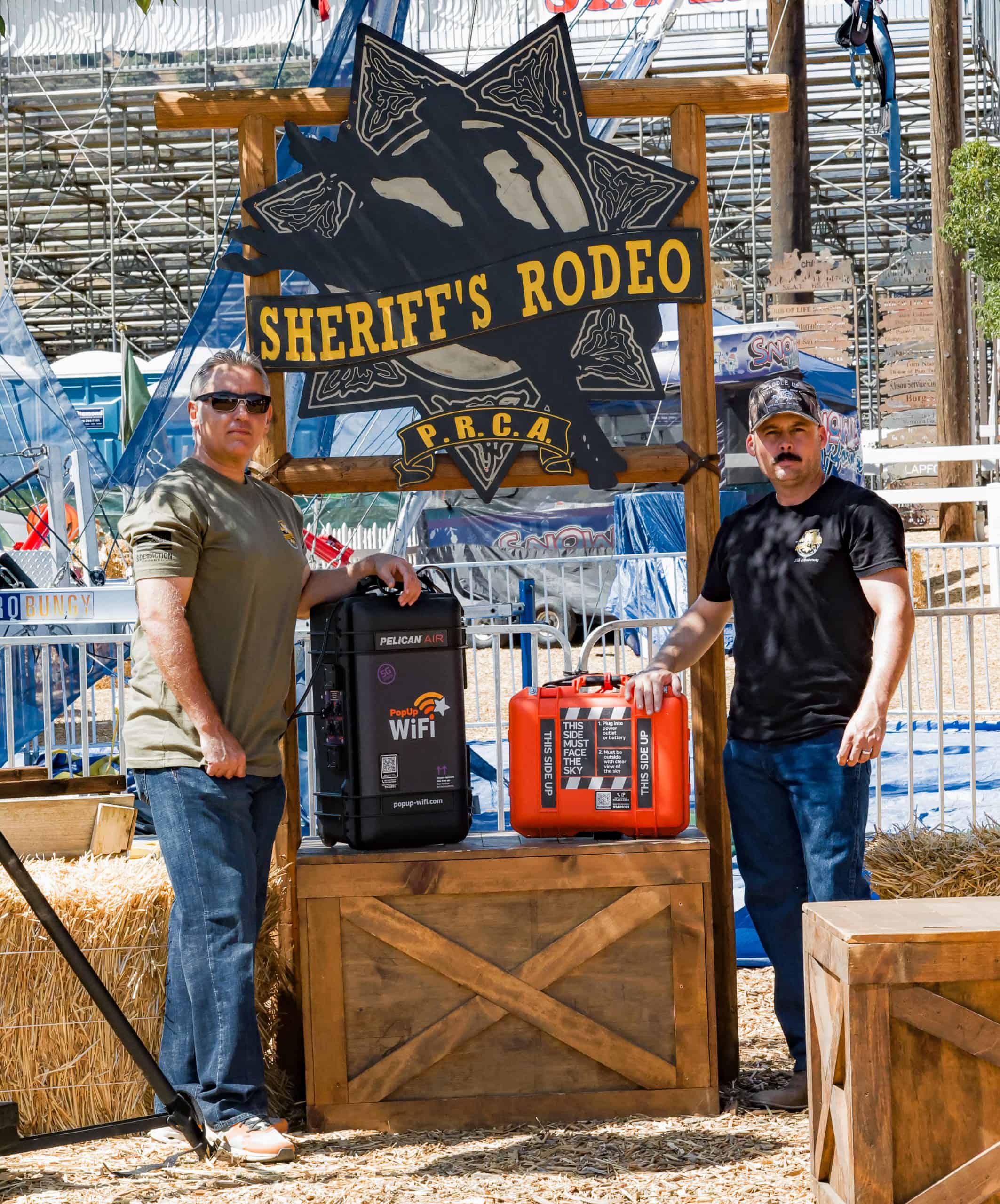 Two officers standing at the entrance of the Sheriff's Rodeo next to a PopUp WiFi Titan and StarCell units which they will use for their event internet for the sporting event.