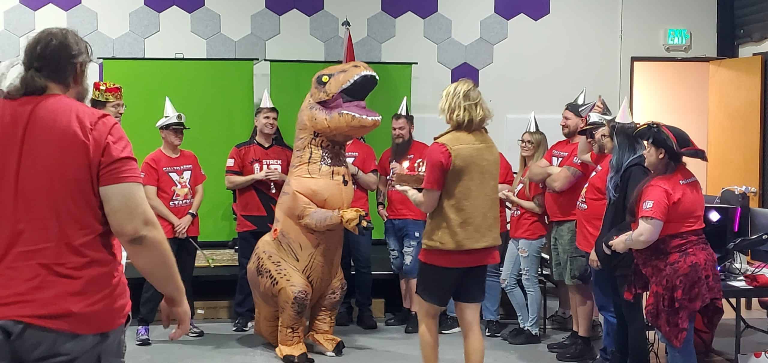 Streamers celebrating around a dinosaur costume with laughter and party hats to celebrate the 10th anniversary of StackUp