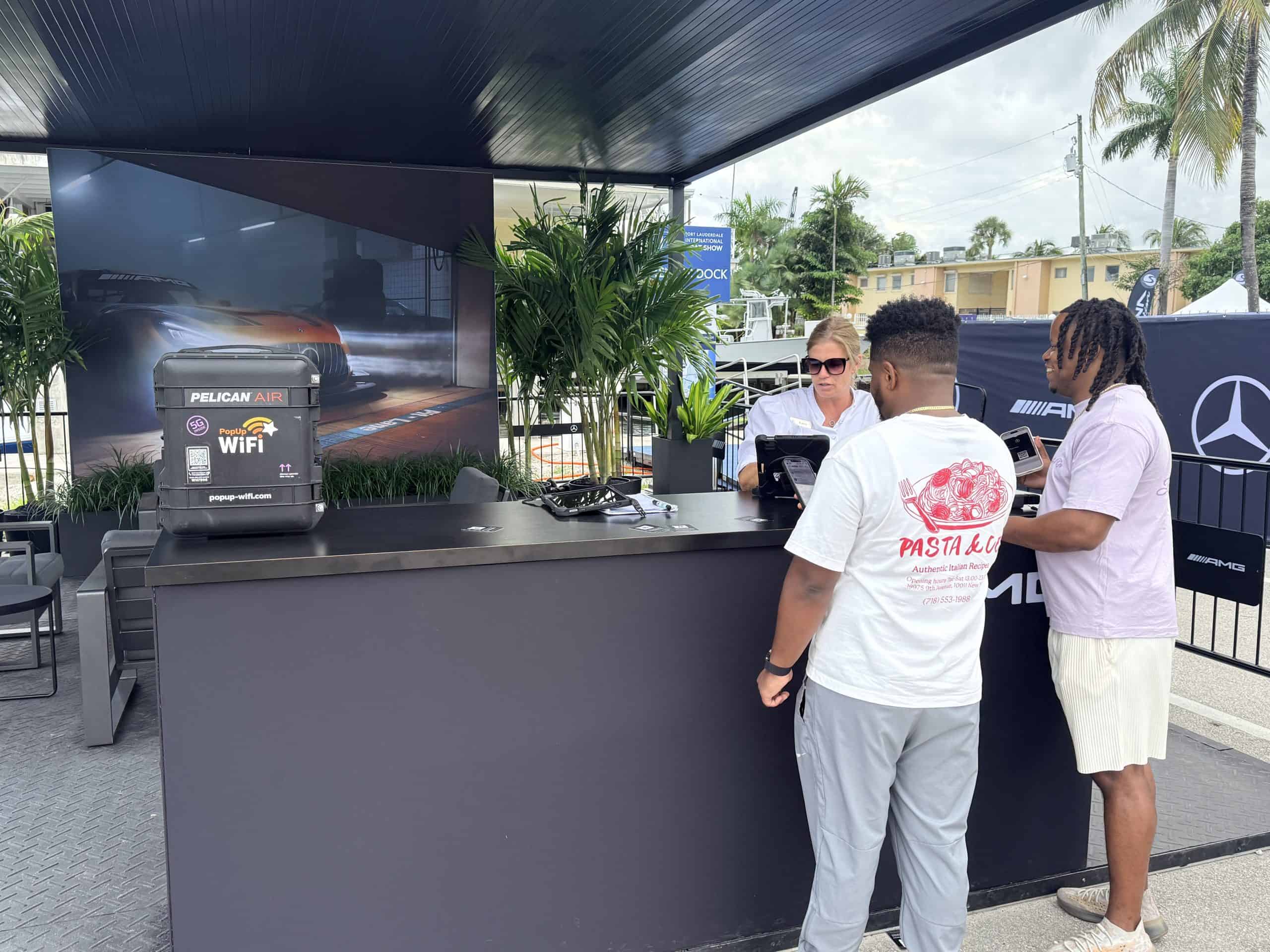 Woman checking in two men at Fort Lauderdale with PopUp WiFi Event WiFi unit in the foreground.