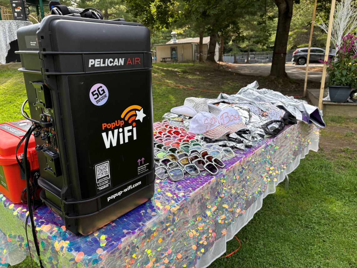 A PopUp WiFi event WiFi rental unit on a sequin table of rhinestone sunglasses and party hats at Storrs Pond Recreation Area, New Hampshire