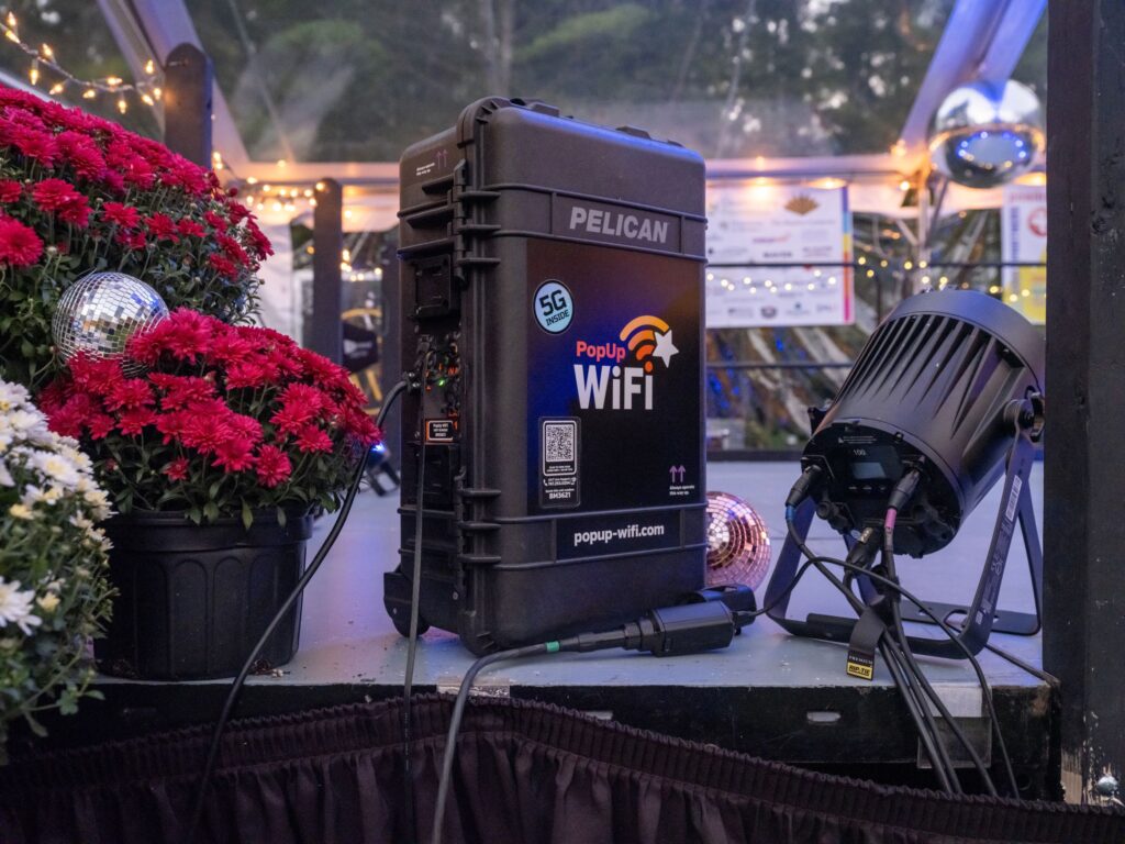 A PopUp WiFi 5G unit on the edge of a tented stage among red mums, disco balls and stage lights at Sweat For Good Games, New Hampshire