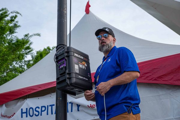 Man setting up event internet unit on a post at an outdoor festival.