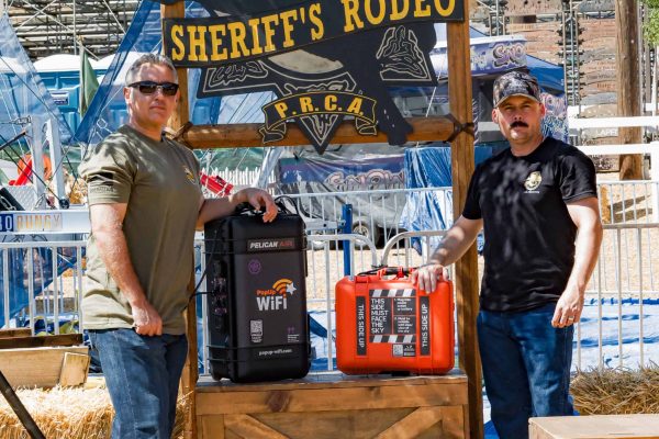 Two officers standing at the entrance of the Sheriff's Rodeo next to a PopUp WiFi Titan and StarCell units which they will use for their event internet for the sporting event.